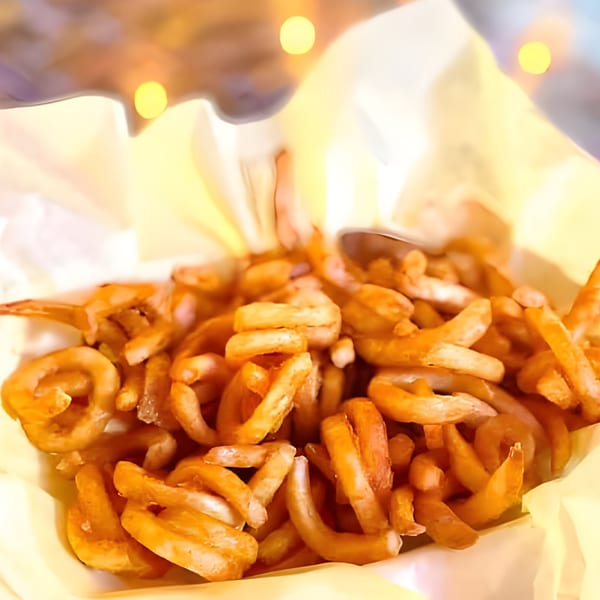 A close-up of golden-brown curly fries in a paper-lined basket at Nicky Ds Crowley.