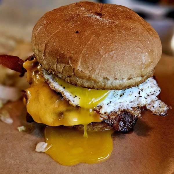 A Nicky Ds burger with melted cheese, bacon, and a fried egg with a runny yolk.