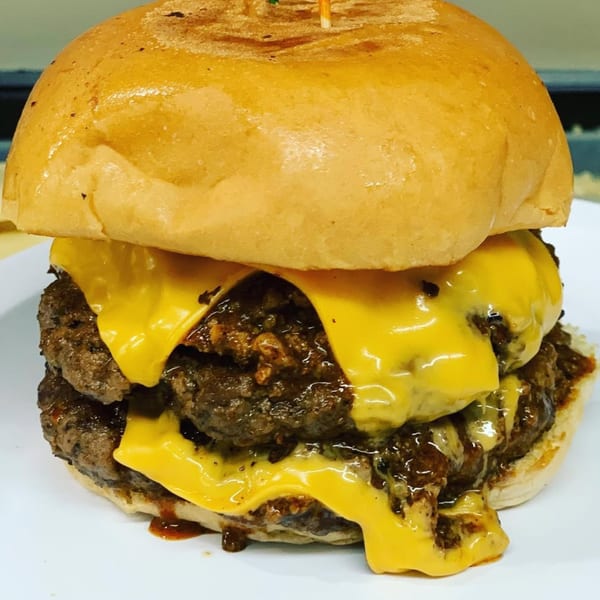 A double cheeseburger from Nicky Ds Crowley, with melted cheese and chili, on a white plate.