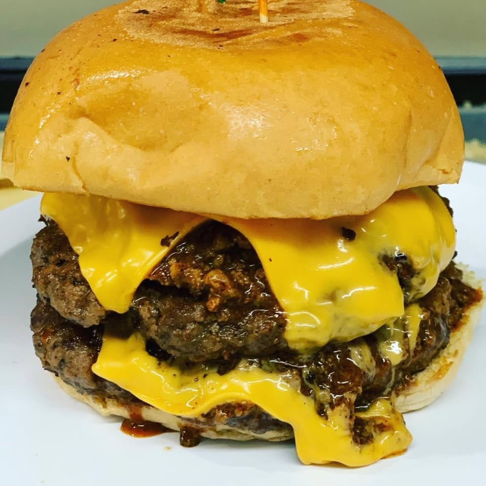 A double cheeseburger from Nicky Ds Crowley, with melted cheese and chili, on a white plate.
