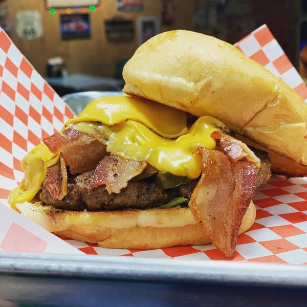 A Nicky Ds Crowley bacon cheeseburger with melted cheese and crispy bacon on a red and white checkered paper.