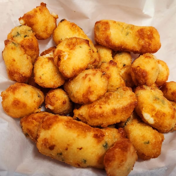 Close-up of golden-brown fried cheese curds with visible melted cheese, served in a white paper-lined basket.