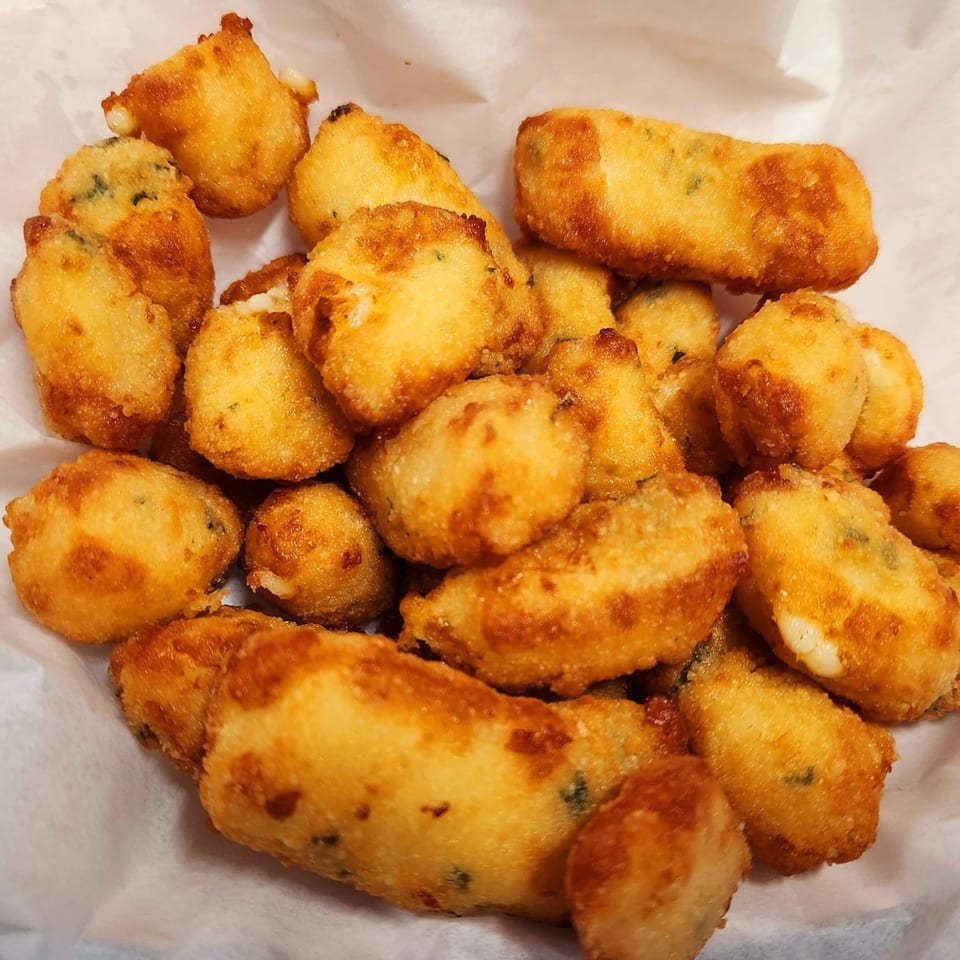 Close-up of golden-brown fried cheese curds with visible melted cheese, served in a white paper-lined basket.