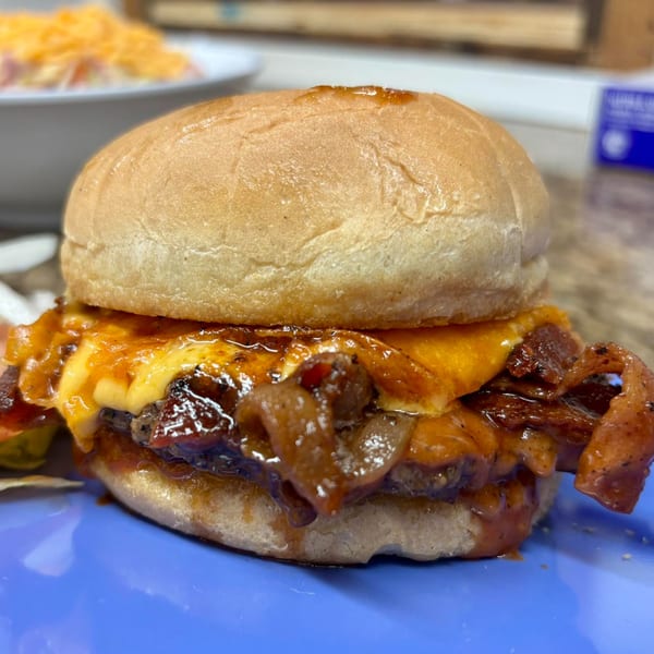 Close-up of a Nicky Ds burger with melted cheese, caramelized onions, and bacon on a blue plate.