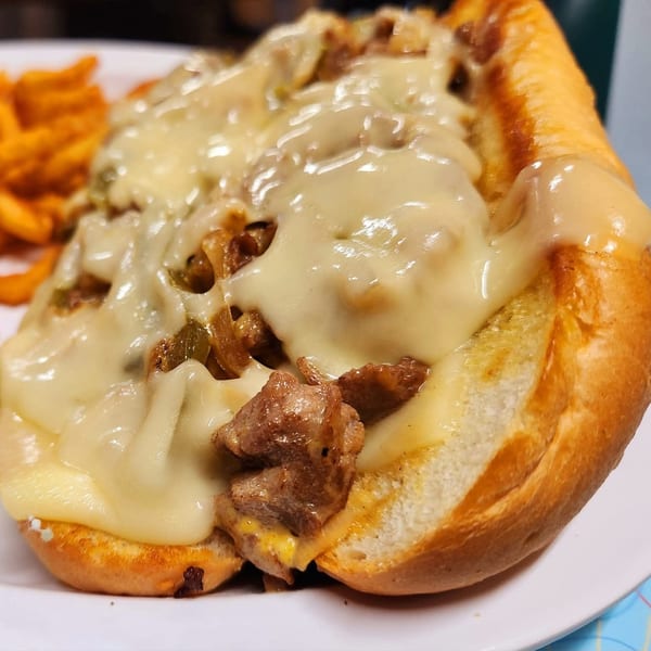 A Nicky Ds cheesesteak sandwich, loaded with melted cheese, steak, and onions, with curly fries.
